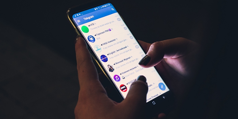 Vista angolare dimezzata di una ragazza che fa tap sull’icona di Telegram con il suo iPhone