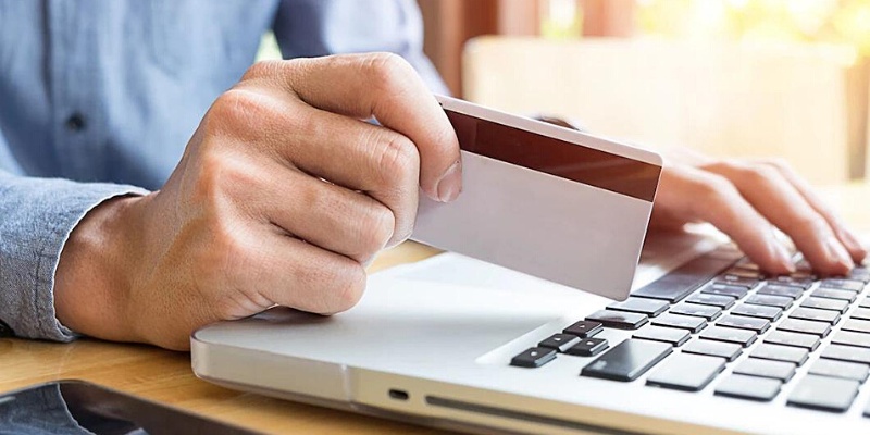 Vista angolare parziale di un uomo che tiene in mano una carta di credito mentre utilizza la tastiera del laptop
