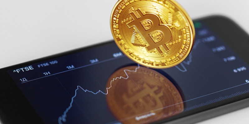 Vista angolare di una moneta Bitcoin sopra il touchscreen dell’iPhone – Piccoli investimenti nel trading