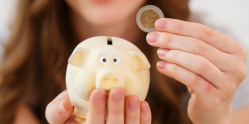 Primo piano di una ragazza che tiene in mano una moneta da 2 euro e un salvadenaio a forma di porcellino – Guadagnare online con pochi euro
